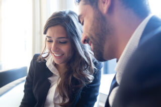 A woman and a man, both smartly dressed in business attire,  viewing some documents together.